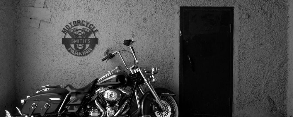 Motorcycle metal sign hung on wall of a garage, above a parked Harley Davidson motorcycle. Sign says "Motorcycle Parking - SMITH's".