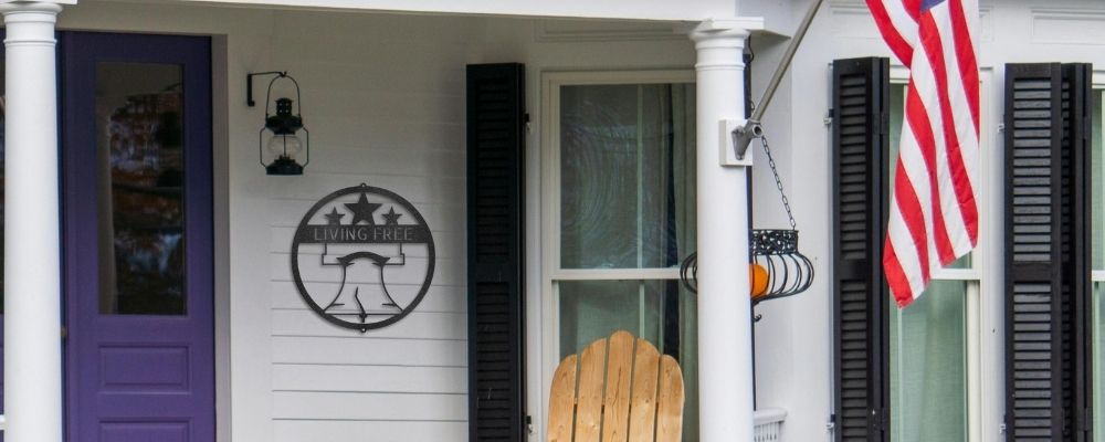 Patriotic metal wall art made for use indoor and outdoor. Liberty Bell design hung on the outside wall of a home with the USA Flag in view.